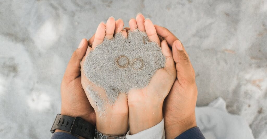 Close-up of a couple holding wedding rings in sand, symbolizing love and union.