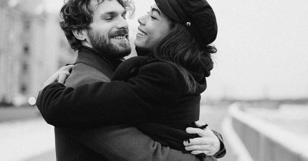 A joyful couple embraces on a snowy day, capturing love and happiness in black and white.